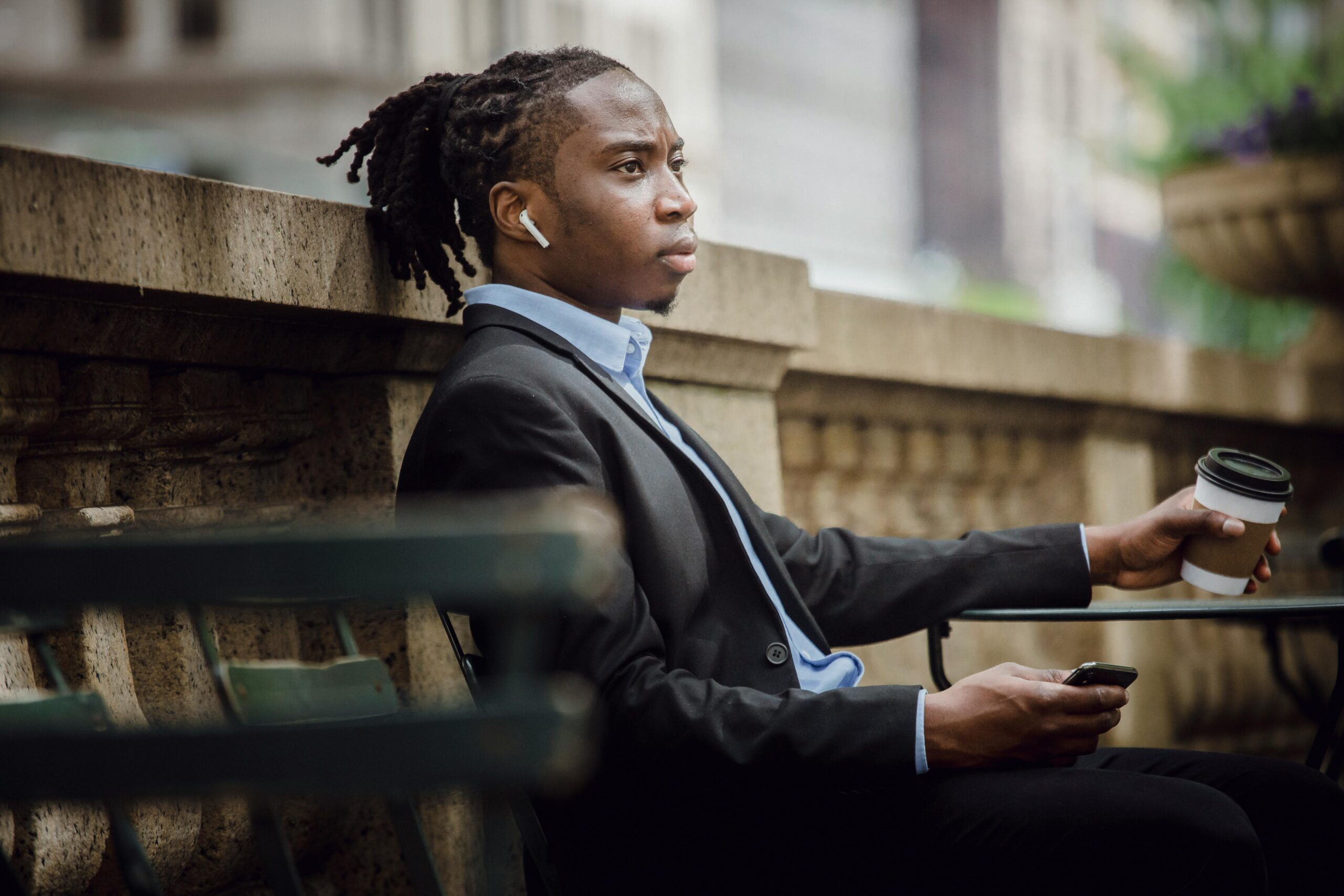 A young professional man in a suit enjoys coffee while listening to music outdoors.